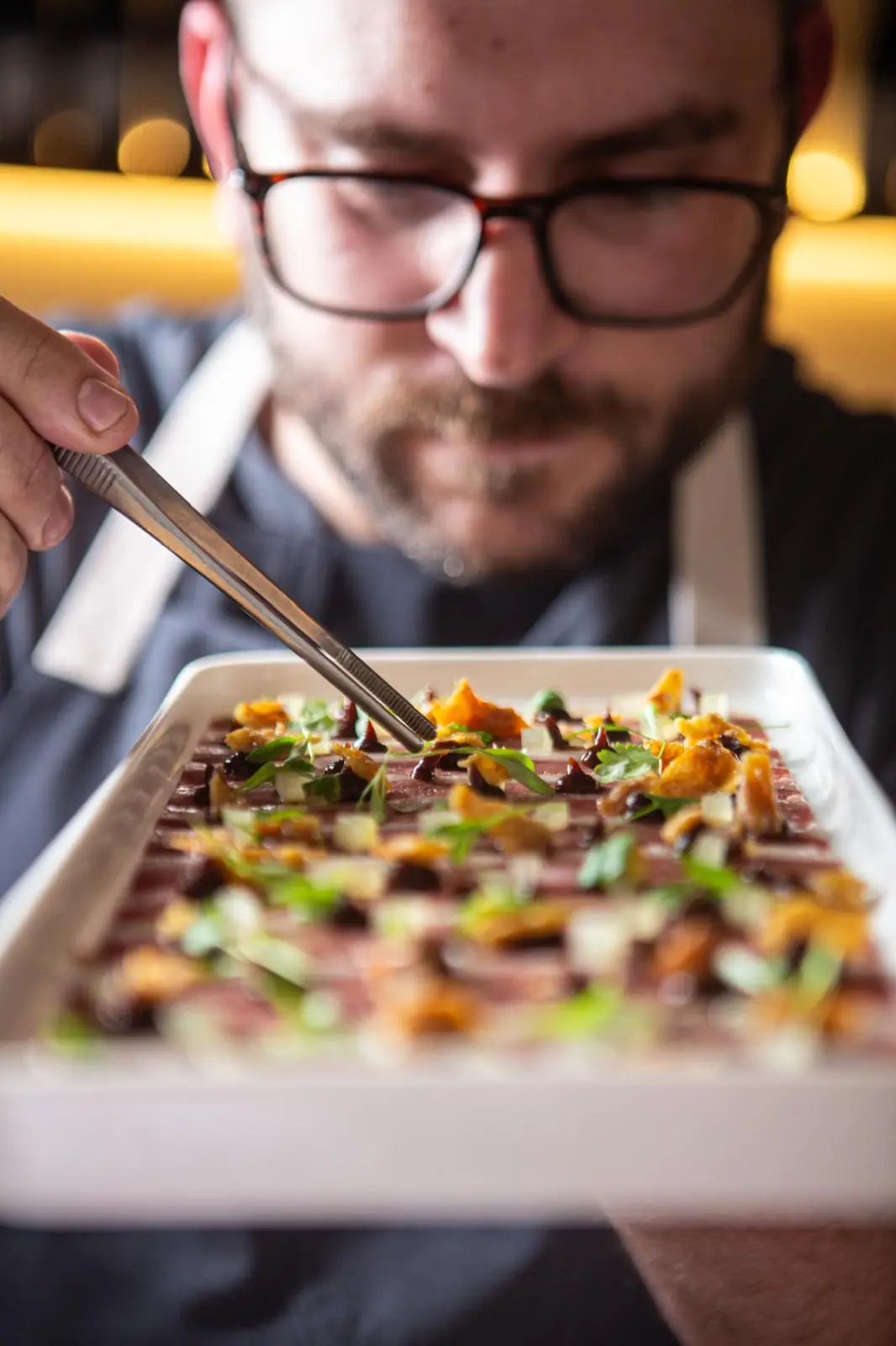Manos del chef terminando un plato con hierbas frescas en Partager